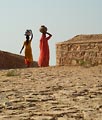 Two women carrying water home, a daily household chore.