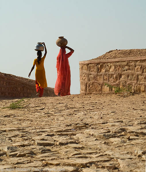 Two women carrying water home, a daily household chore.